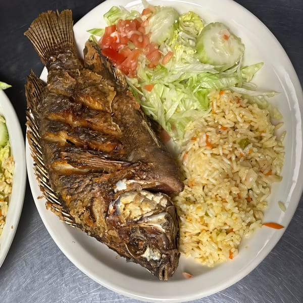 A whole fried fish, rice, and a fresh salad with lettuce, tomatoes, and cucumbers on a white plate.