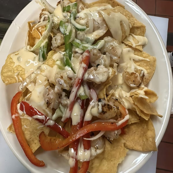 Shrimp nachos with melted white cheese, green and red bell peppers, and onions on a white plate.