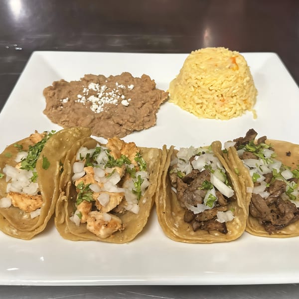 Four La Bamba tacos, two chicken and two steak, with rice and refried beans on a white plate.