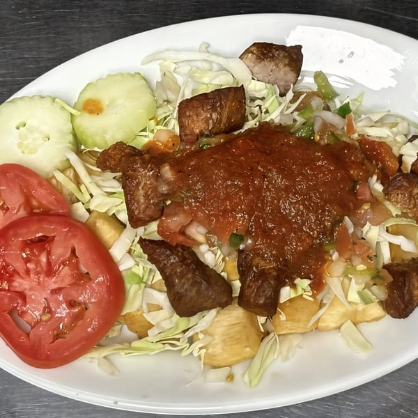 La Bamba's Mexican dish with meat, red sauce, cabbage, tomatoes, and cucumbers on a white plate.