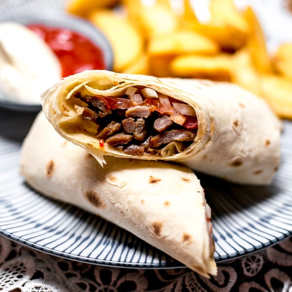 Two La Bamba burritos, one cut open to show meat, onions, and tomatoes, with fries and sauces.