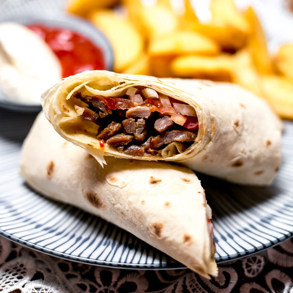Two La Bamba burritos, one cut open to show meat, onions, and tomatoes, with fries and sauces.
